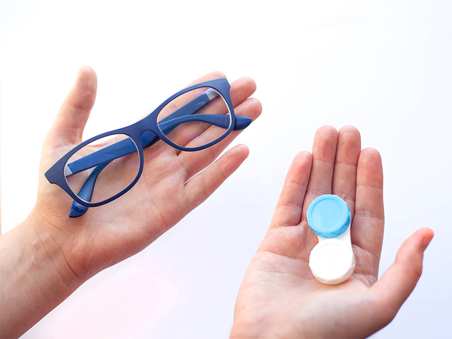 spectacles or contact lenses - female hands holding eyeglasses and contact lenses and choosing