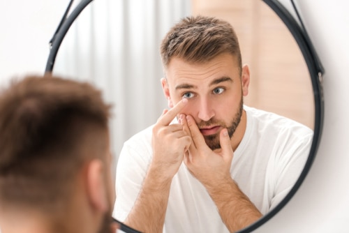 Young man putting in contact lenses near mirror