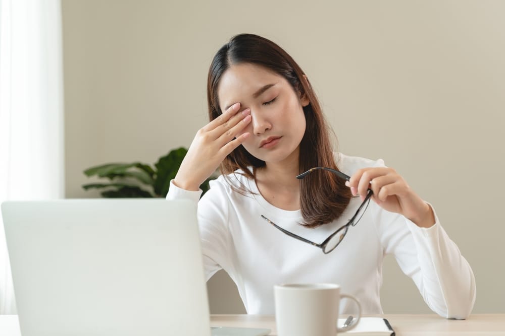 Woman working at her desk rubs her eyes in misguided attempt to relieve a dry eye flare