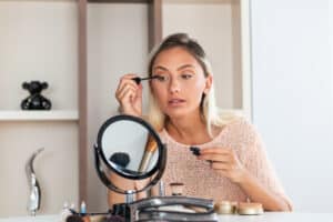 Woman applying mascara and makeup while looking in a mirror