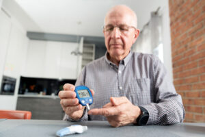 senior man with glucometer checking blood sugar level at home